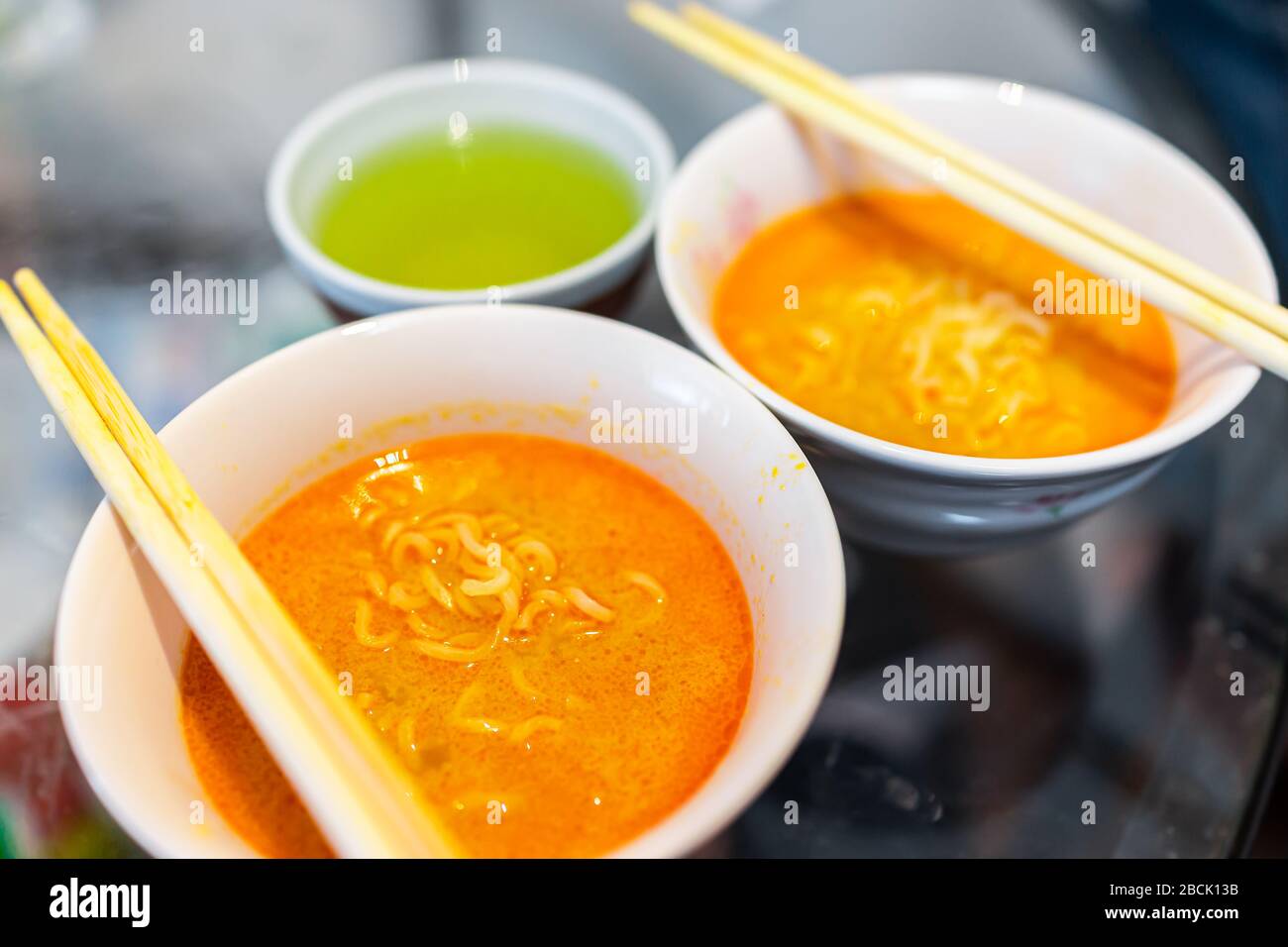 Macro closeup di due piccanti scodelle zuppa di ramen rosso con bastoni cucina asiatica giapponese e tè verde Foto Stock