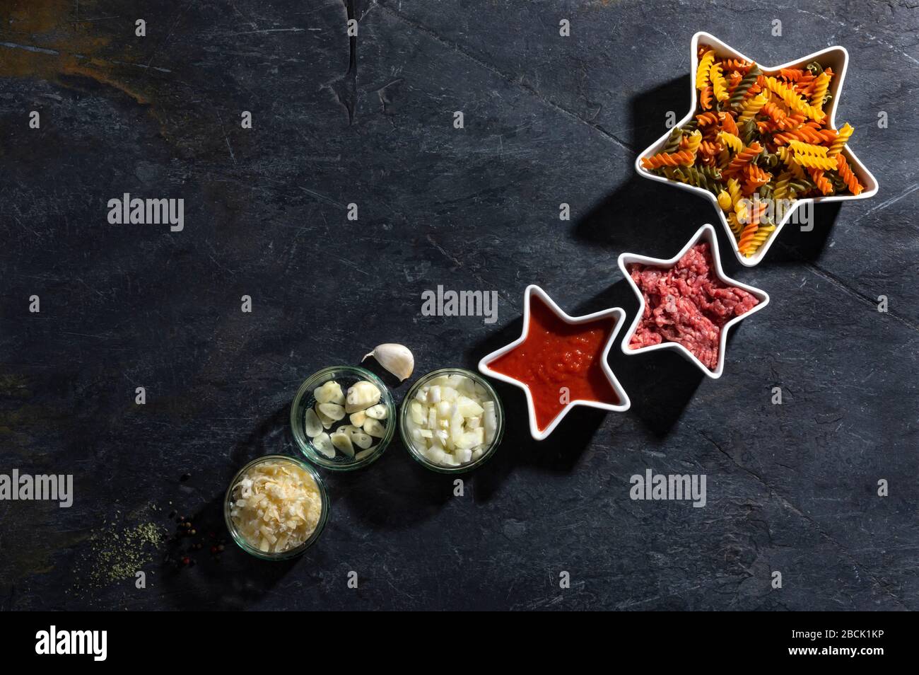 Pasta secca, carne e verdure su un tavolo con sfondo di ardesia scura, con spazio per le copie. Concept star composizione fusilli e ricetta bolognese. Foto Stock