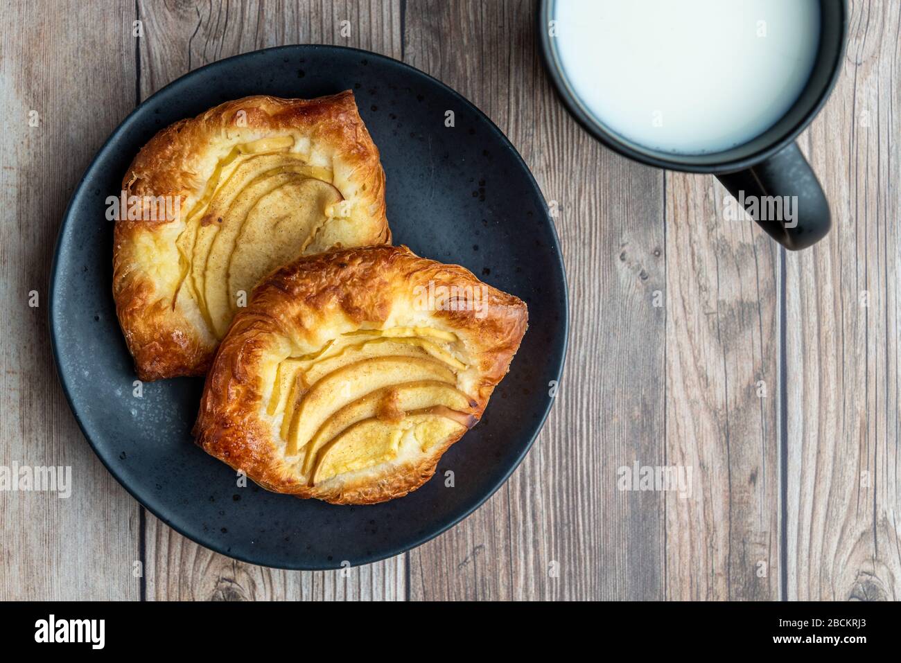 Crostate di mele fresche su piatto nero, tazza di latte freddo, fondo in legno Foto Stock