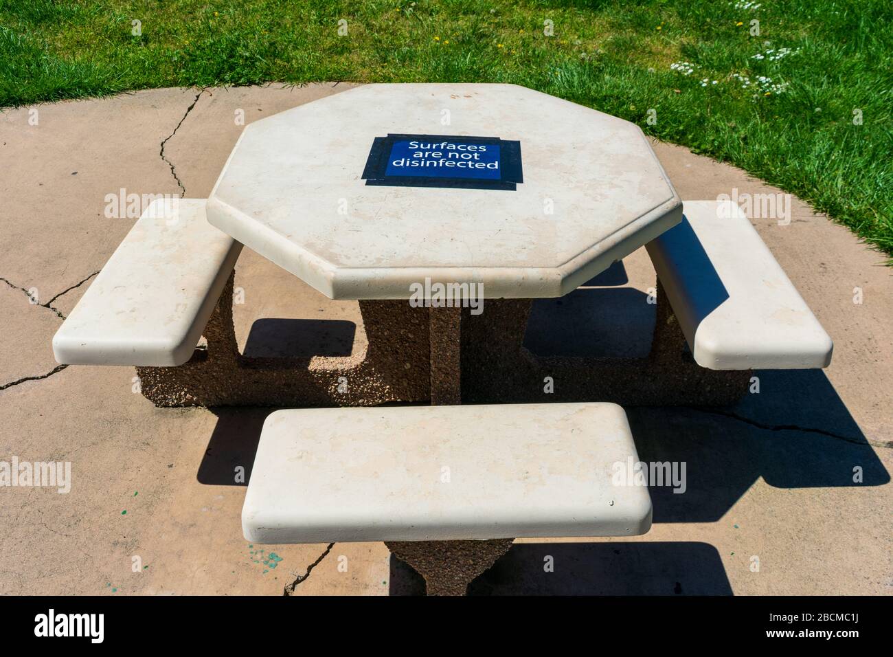 Tavolo da picnic in cemento nel parco pubblico con superficie non disinfettata cartello di avvertenza temporaneo attaccato al piano. Foto Stock