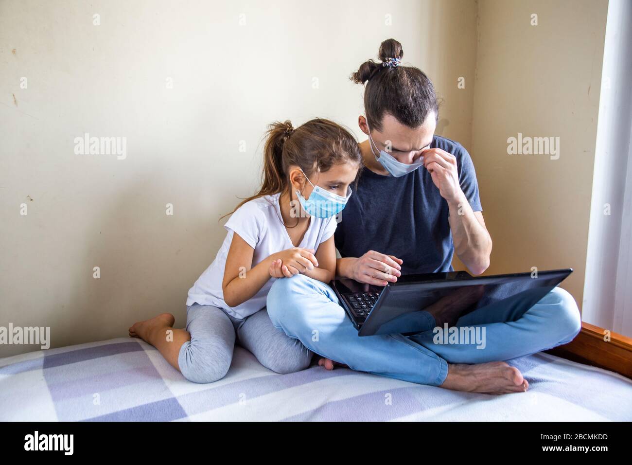 Rimani al sicuro a causa della pandemia di coronavirus. Padre e piccolo papà che si siedano con il laptop. La famiglia insieme. Buon lavoro e studio a distanza da casa Foto Stock