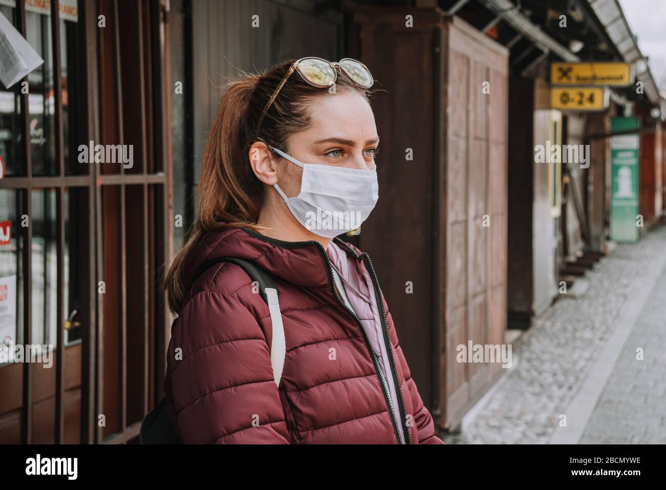 Donna proprietario con maschera dietro negozio di vestiti in strada vuota città a causa di coronaviri epidemia covid-19 Foto Stock