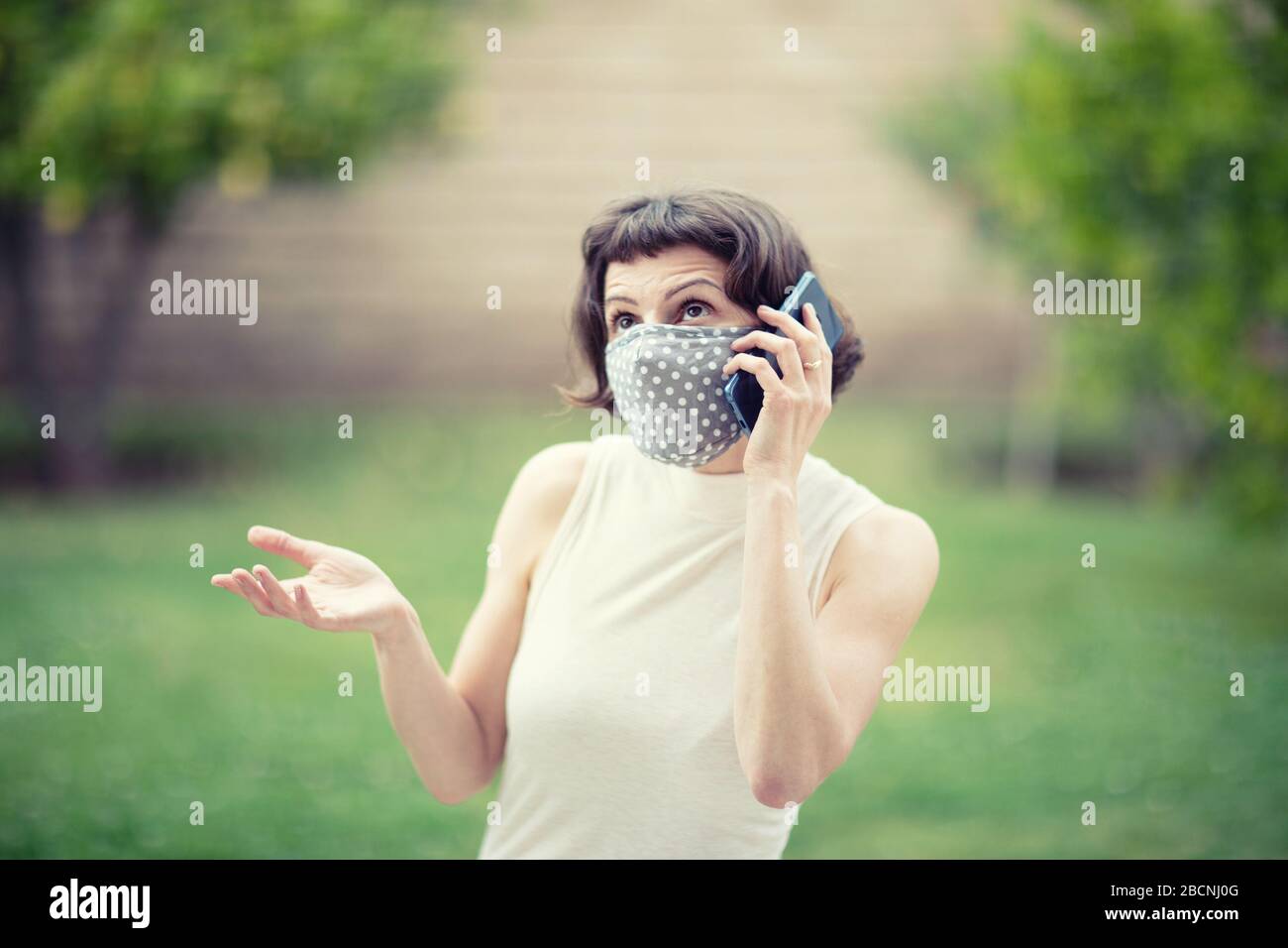 Ragazza giovane in una maschera facciale mentre parla al telefono all'esterno. La nuova raccomandazione del governo degli Stati Uniti ha consigliato a tutti di indossare maschere in pubblico d Foto Stock