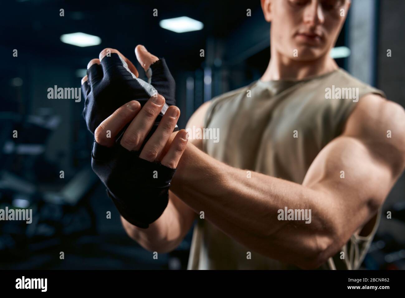 Raccolto di bel bodybuilder in abbigliamento sportivo e guanti che si allungano la parte superiore del corpo in club sportivo. Vista laterale dello sportivo muscolare in guanti che si posano a vuoto Foto Stock