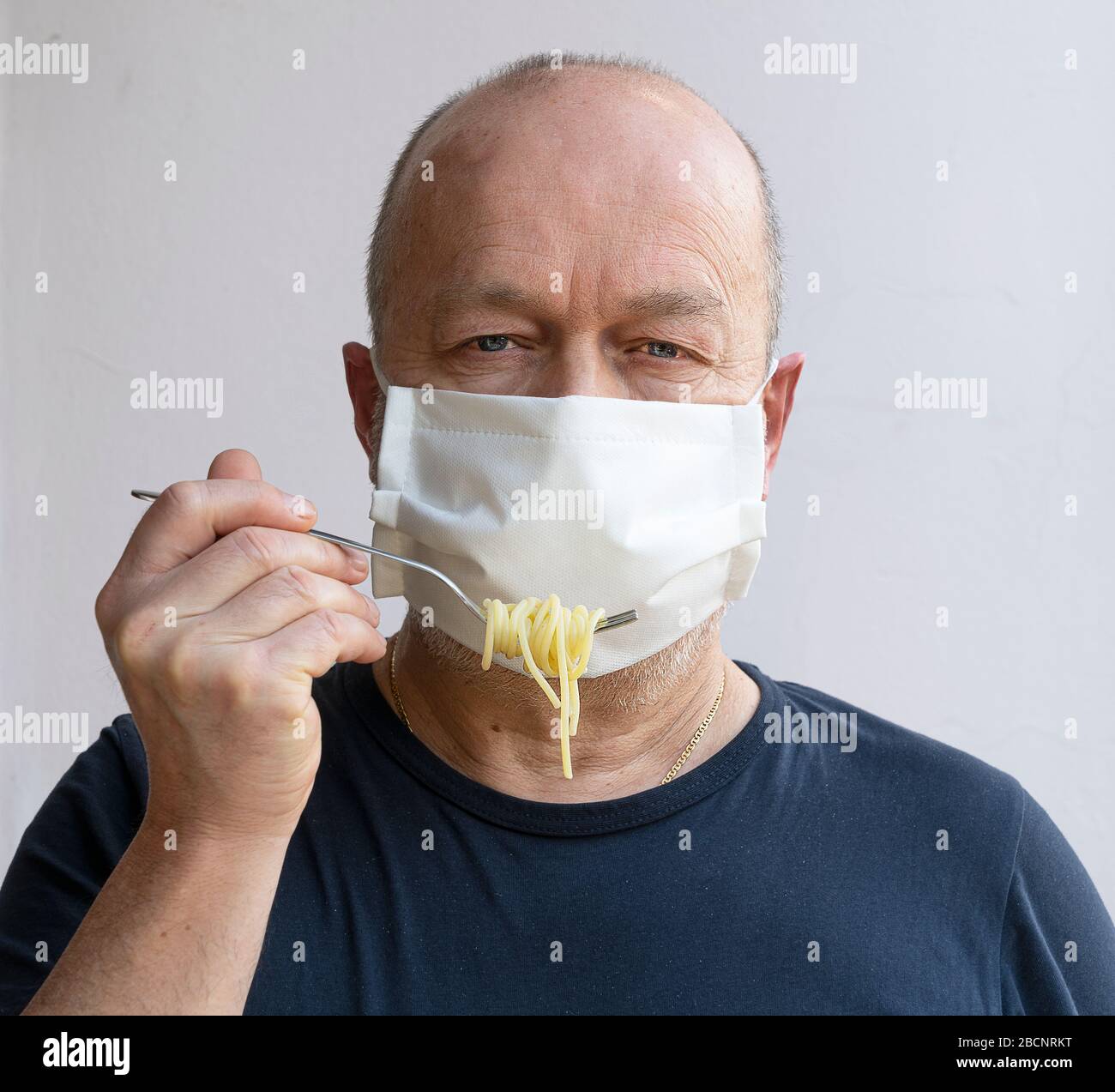 Mangi la pasta nel periodo del coronavirus con una maschera protettiva Foto Stock