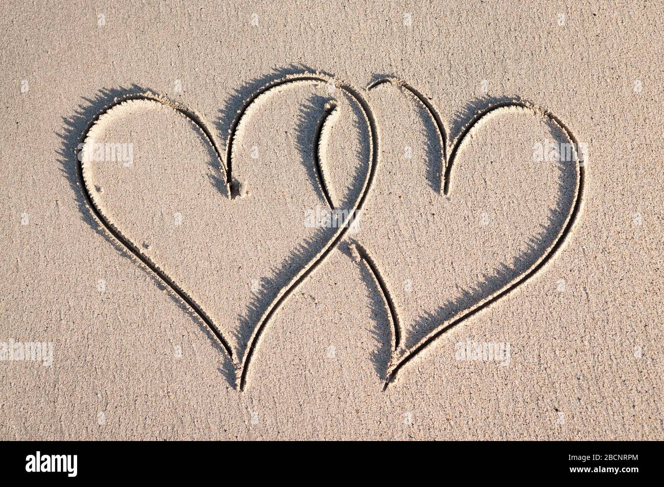Coppia di cuori scritti a mano disegnati in un'interbloccaggio in sabbia liscia su una spiaggia soleggiata Foto Stock