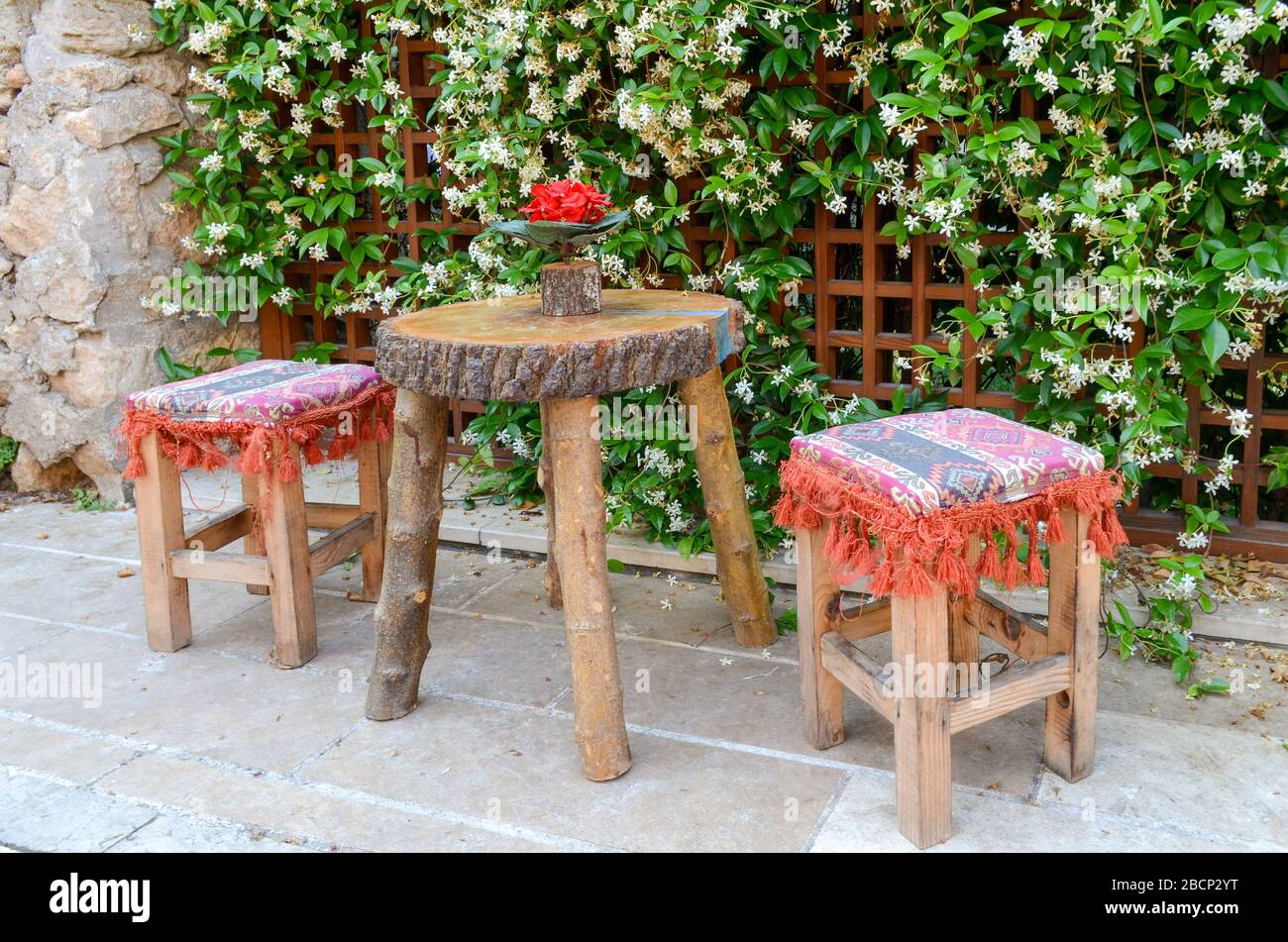 Due sgabelli di legno e un piccolo tavolo sulla parete di fondo con gelsomino fiorito. Stile orientale Foto Stock