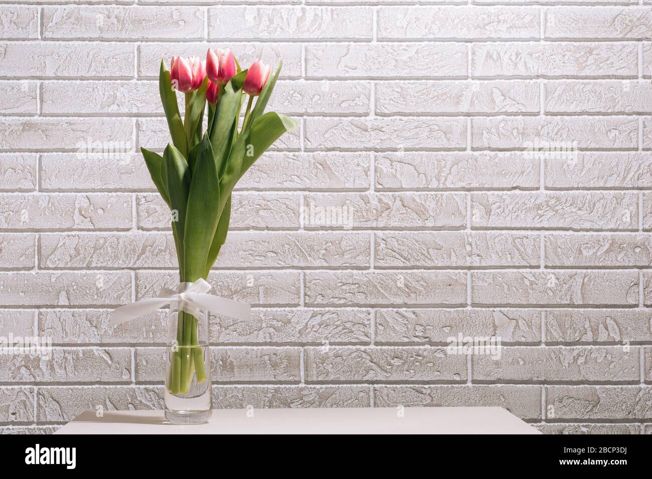 Bouquet rosa tulipano in vaso trasparente su fondo bianco in mattoni. Foto Stock