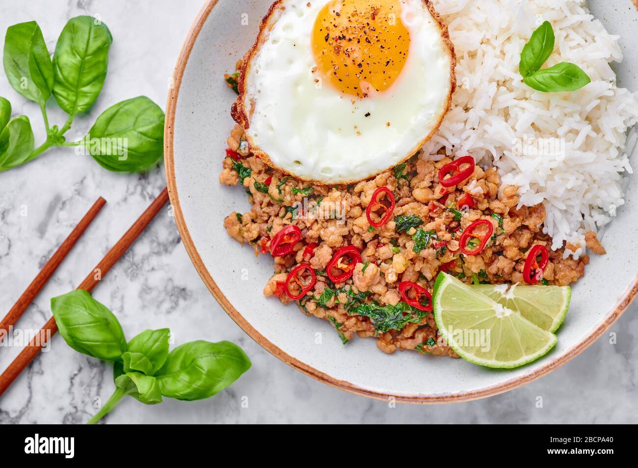 Pad Krapow Gai - pollo al basilico tailandese con riso e uova fritte su sfondo di marmo bianco. Pad Krapow è un piatto di cucina tailandese con pollo tritato o maiale me Foto Stock