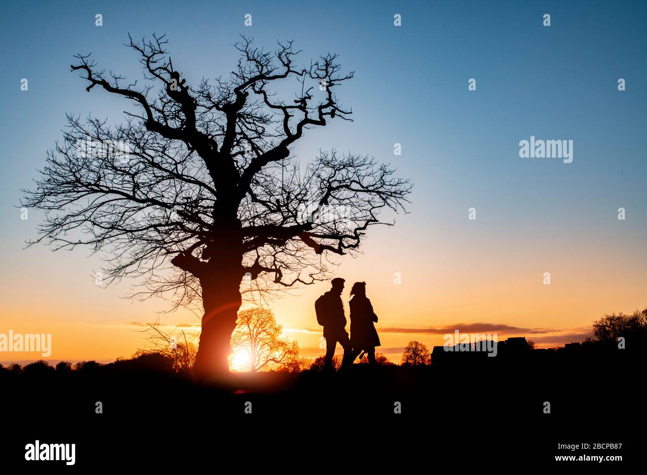 Gli amici si tengono in forma con una passeggiata su Clapham Common (sotto blocco per Corona virus Covid 19 restrizioni) sotto un drammatico tramonto nel marzo 2020 Foto Stock