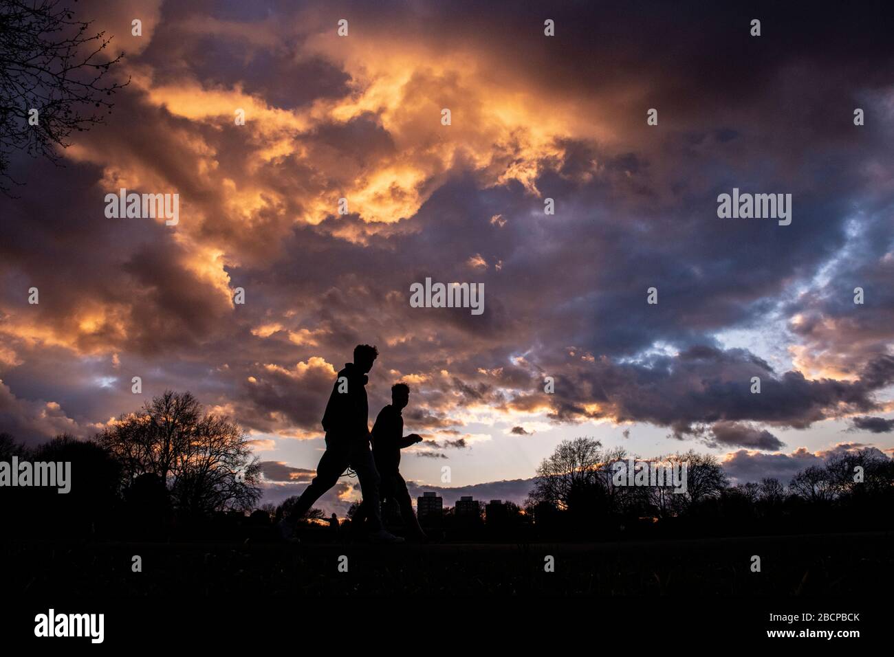 Gli amici si tengono in forma con una passeggiata su Clapham Common (sotto blocco per Corona virus Covid 19 restrizioni) sotto un drammatico tramonto nel marzo 2020 Foto Stock