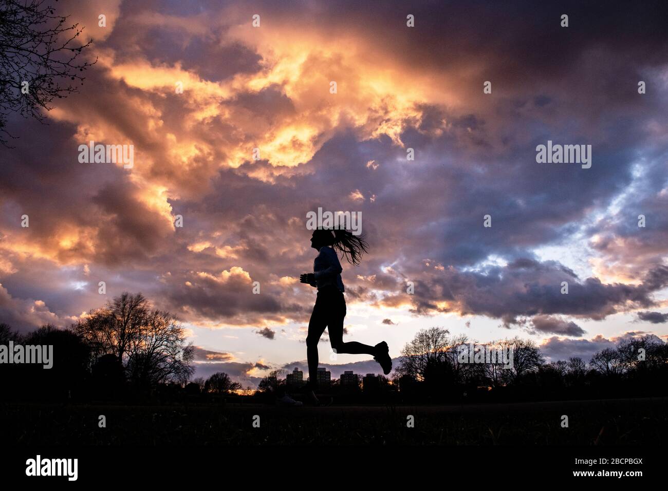 Running e mantenersi in forma (sotto blocco per Corona virus Covid 19 restrizioni) sotto un drammatico tramonto nel marzo 2020 Foto Stock Running e mantenersi in forma (sotto blocco per Corona virus Covid 19 restrizioni) sotto un drammatico tramonto nel marzo 2020 Foto Stock