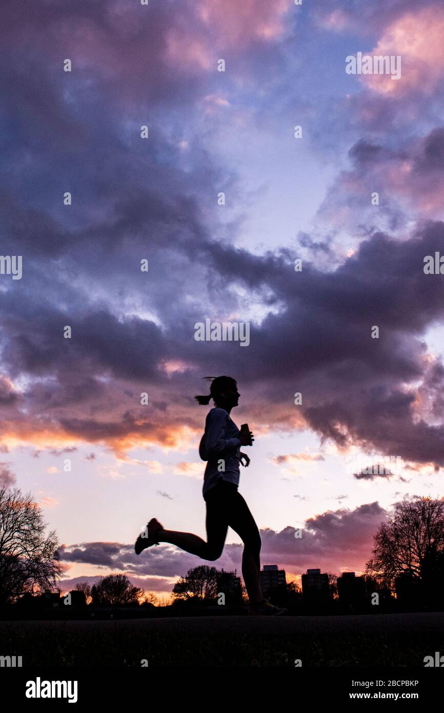 Running e mantenersi in forma (sotto blocco per Corona virus Covid 19 restrizioni) sotto un drammatico tramonto nel marzo 2020 Foto Stock Running e mantenersi in forma (sotto blocco per Corona virus Covid 19 restrizioni) sotto un drammatico tramonto nel marzo 2020 Foto Stock