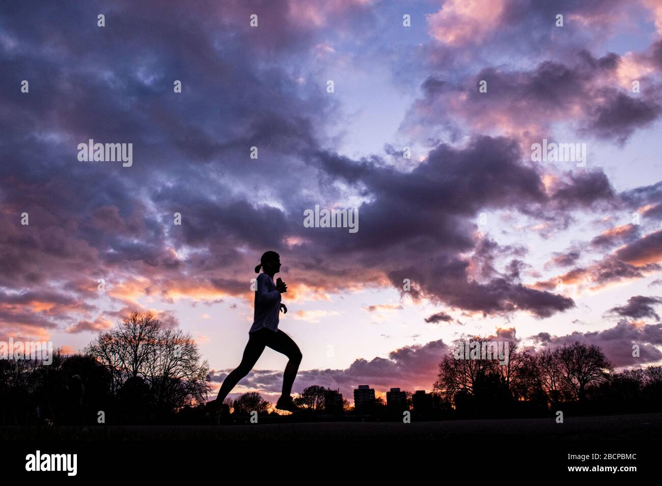 Running e mantenersi in forma (sotto blocco per Corona virus Covid 19 restrizioni) sotto un drammatico tramonto nel marzo 2020 Foto Stock Running e mantenersi in forma (sotto blocco per Corona virus Covid 19 restrizioni) sotto un drammatico tramonto nel marzo 2020 Foto Stock
