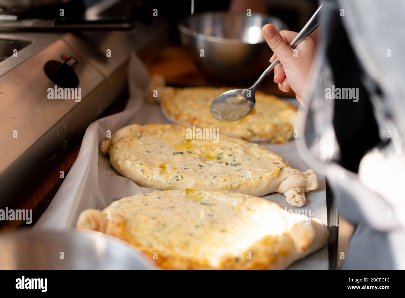 Delizie master class. Primo piano delle mani di persone preparando khachapuri. In stile georgiano tradizionale pane di formaggio. Il cibo in stile georgiano. Grande famiglia irriconoscibile cooki Foto Stock