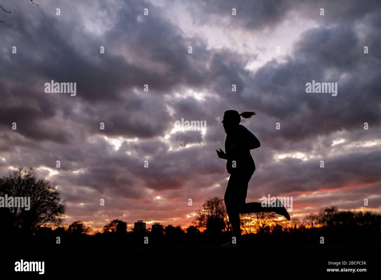 Running e mantenersi in forma (sotto blocco per Corona virus Covid 19 restrizioni) sotto un drammatico tramonto nel marzo 2020 Foto Stock Running e mantenersi in forma (sotto blocco per Corona virus Covid 19 restrizioni) sotto un drammatico tramonto nel marzo 2020 Foto Stock