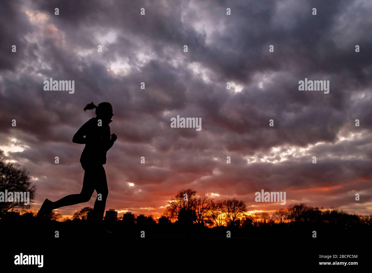 Running e mantenersi in forma (sotto blocco per Corona virus Covid 19 restrizioni) sotto un drammatico tramonto nel marzo 2020 Foto Stock Running e mantenersi in forma (sotto blocco per Corona virus Covid 19 restrizioni) sotto un drammatico tramonto nel marzo 2020 Foto Stock