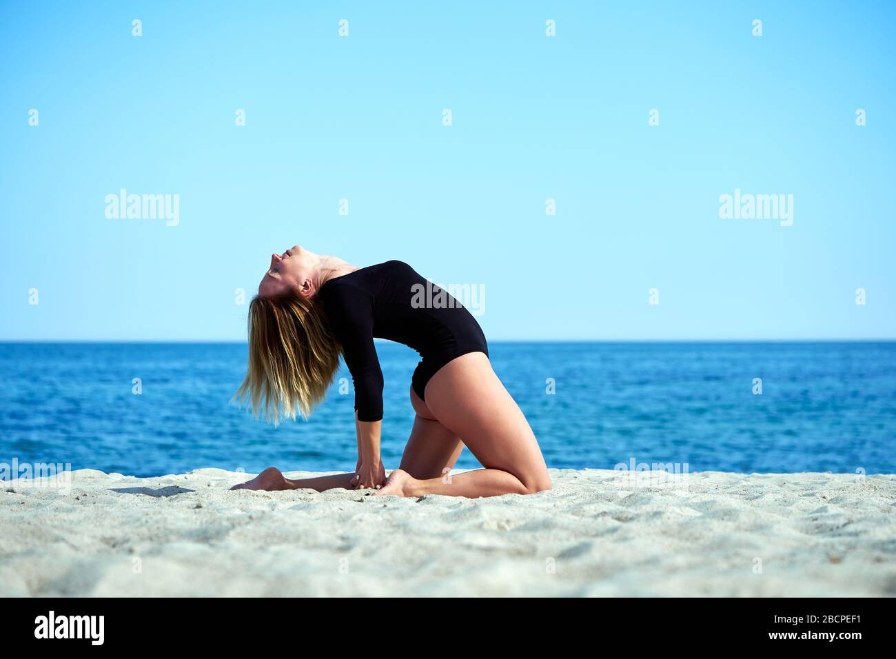 Bella donna pratica yoga sul mare in una giornata di sole. La donna fa esercizi stretching. Foto Stock