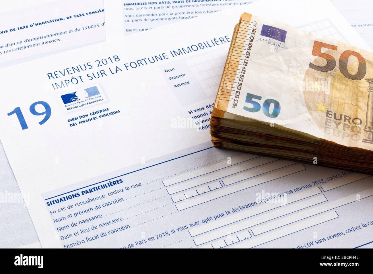 Pila di 50 banconote in euro sulla parte superiore di un modulo di imposta sul patrimonio immobiliare francese (Impôt sur la fortune immobilière). Foto Stock