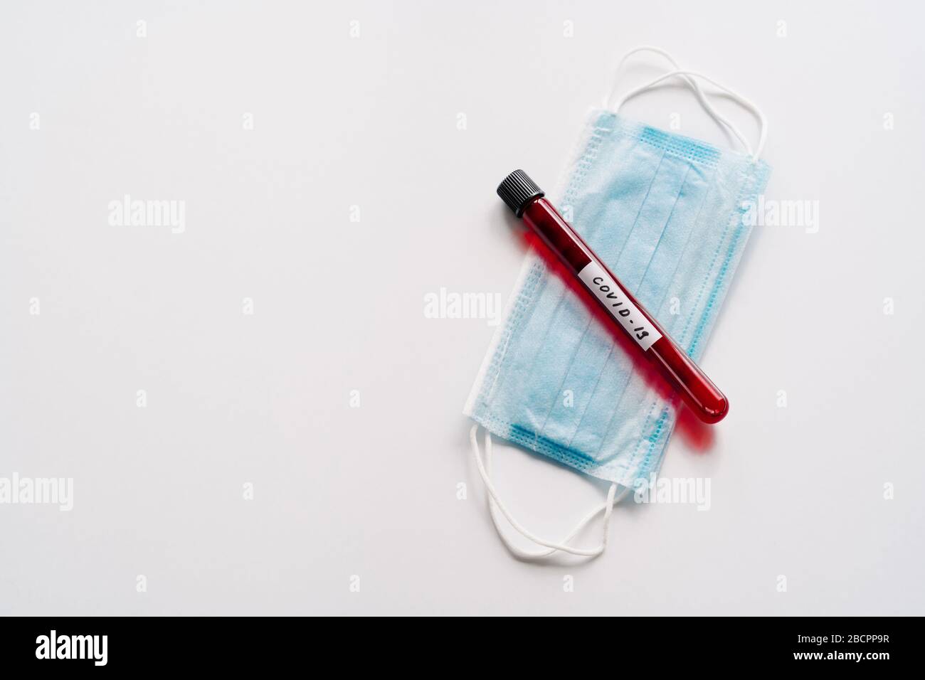Provetta contenente campioni di sangue per analisi o analisi di coronavirus, maschera medica sterile su sfondo bianco. Analisi chimica in laboratorio. BI Foto Stock