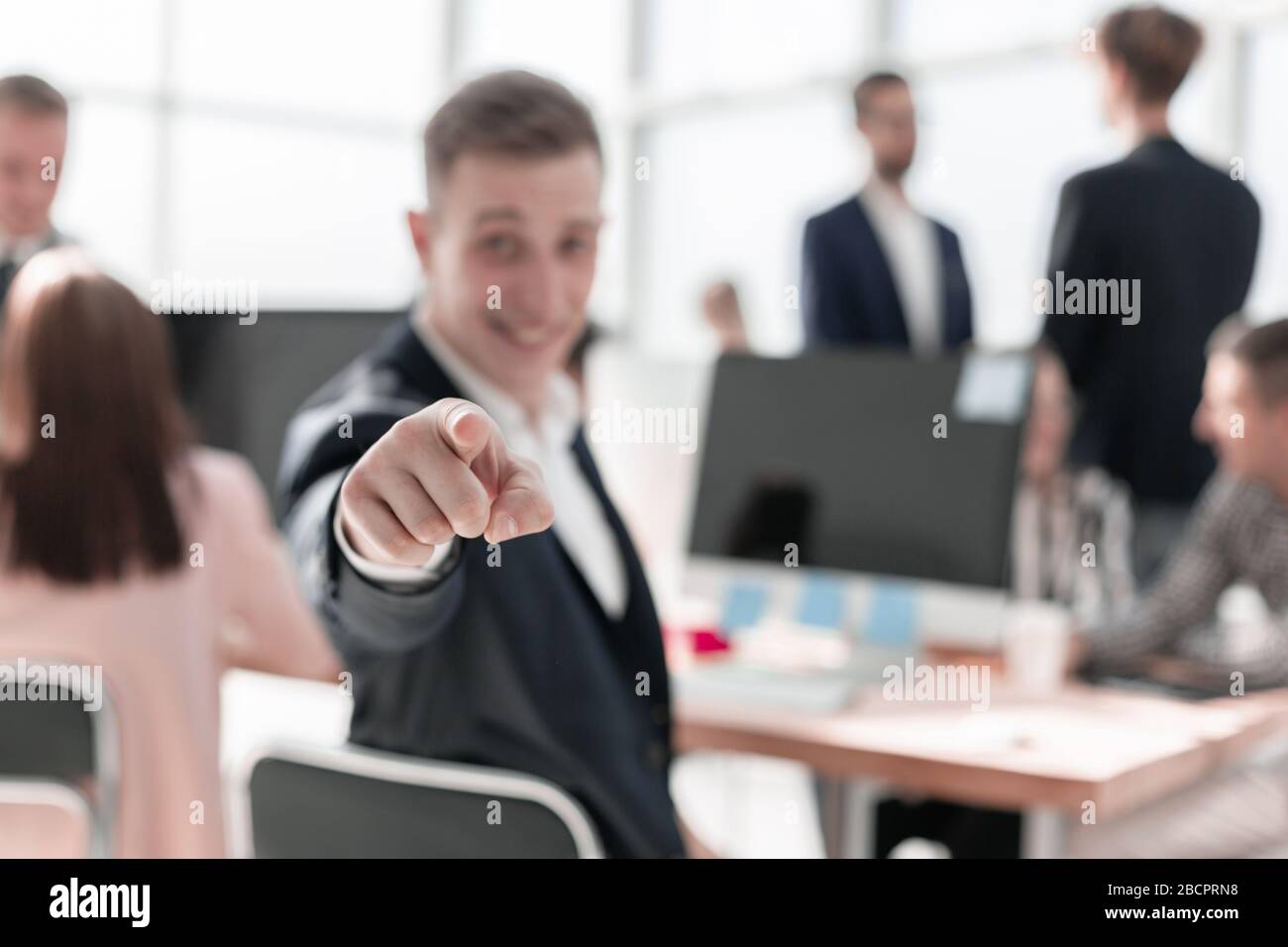 Sorridente giovane impiegato seduto alla sua scrivania e indicando voi Foto Stock