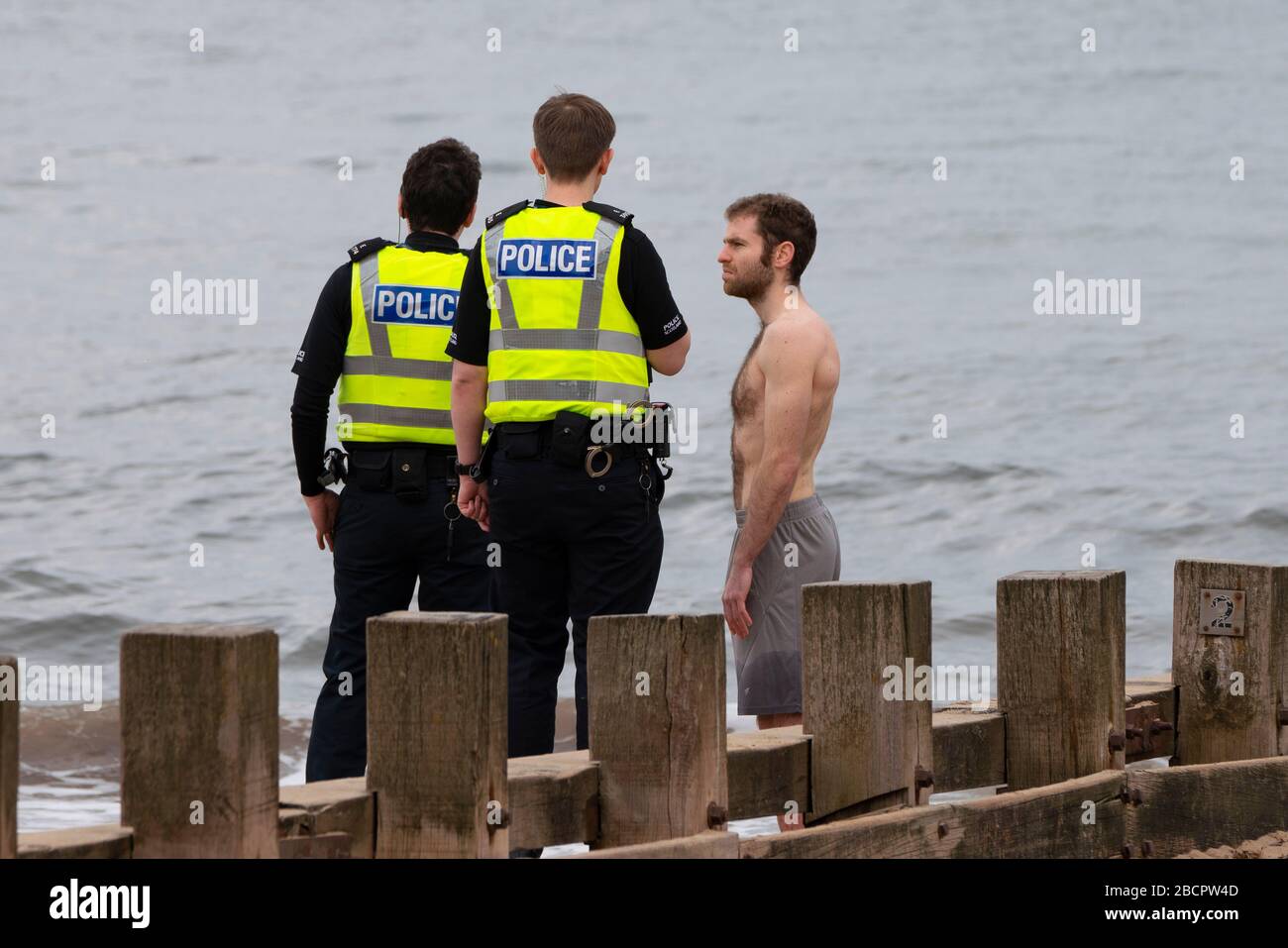 Portobello, Edimburgo, Scozia, Regno Unito. 5 aprile 2020. La seconda domenica del blocco del coronavirus nel Regno Unito il pubblico è al di fuori di prendere il loro esercizio quotidiano. Nella foto. La polizia parla con l'uomo in tronchi sulla spiaggia di Portobello. Dopo la discussione l'uomo fu autorizzato a continuare con la sua nuotata. Iain Masterton/Alamy Live News Foto Stock