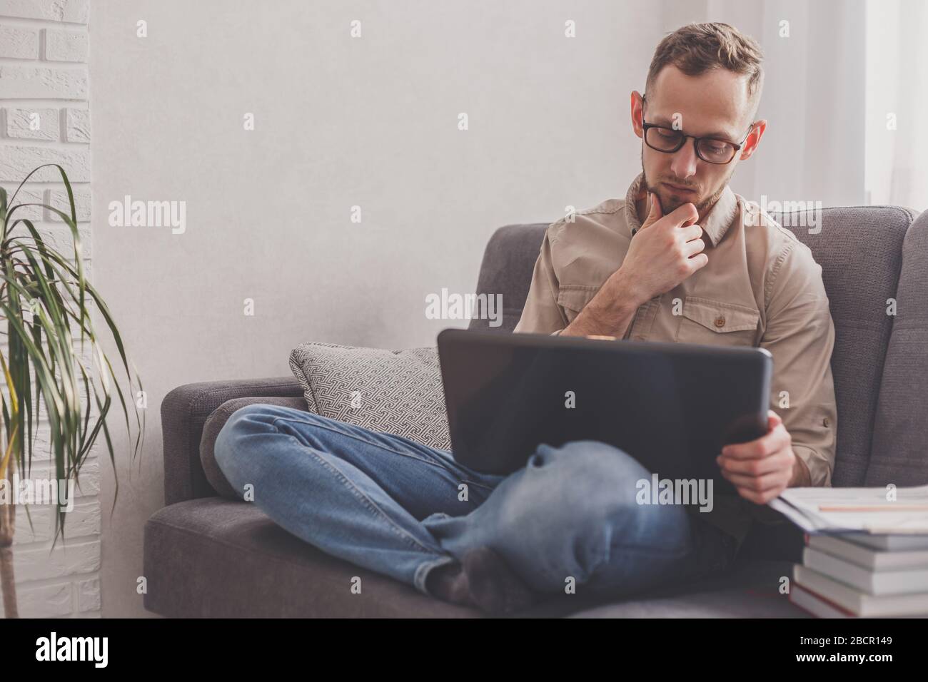 Processo remoto. Uomo che lavora su un computer portatile seduto sul divano a casa. Foto Stock