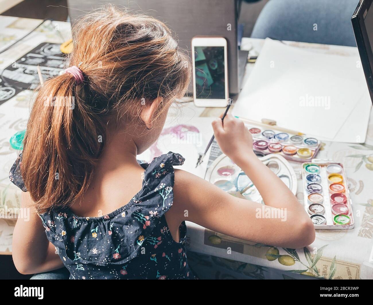 Ragazza disegna con vernici. Idee per le attività con i bambini a casa. Inquadratura verticale. Vista da dietro Foto Stock