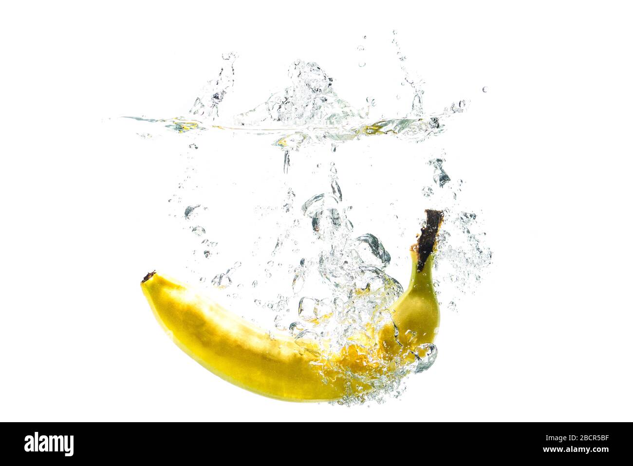 una banana che cade in acqua su uno sfondo bianco con spruzzi. Foto Stock