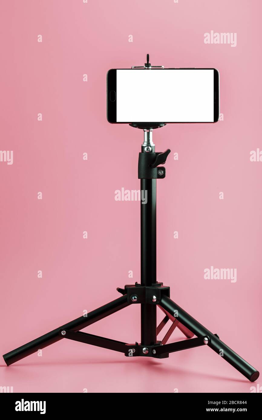 Telefono cellulare montato su un treppiede con un display bianco libero per immagini e testo, sfondo isolato rosa. Foto Stock