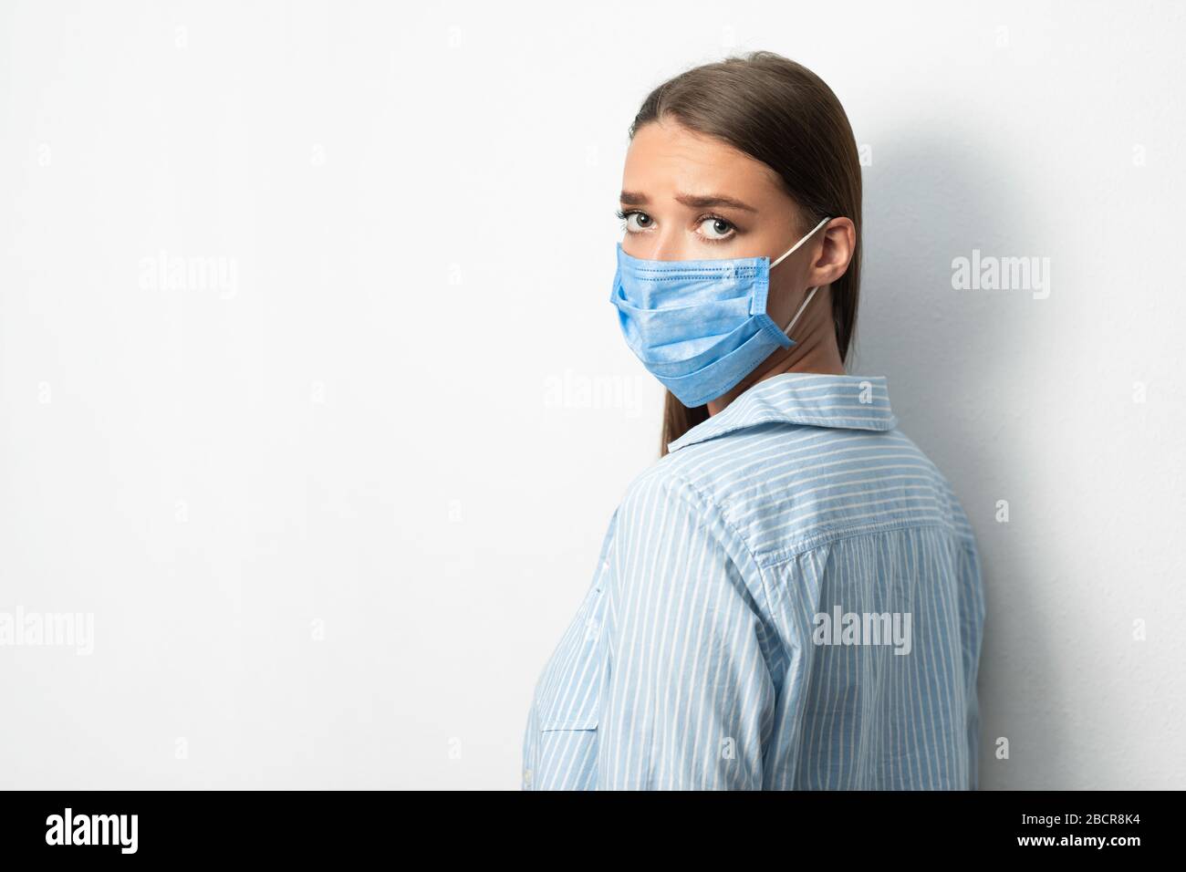 Donna triste che indossa la maschera medica guardando la macchina fotografica, sfondo bianco Foto Stock