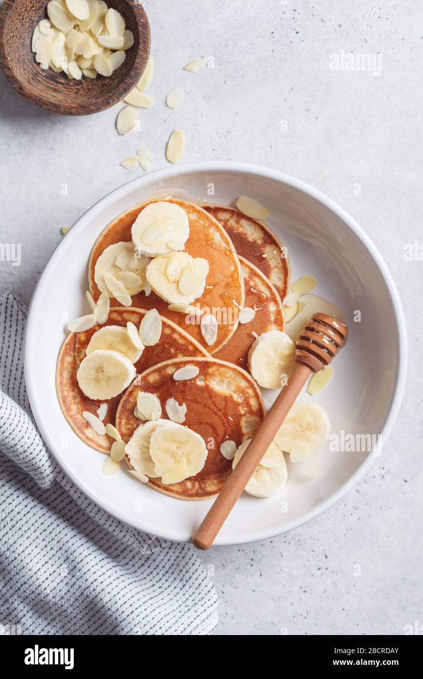 Pancake tradizionali con banana, mandorle e miele in un piatto bianco. Foto Stock