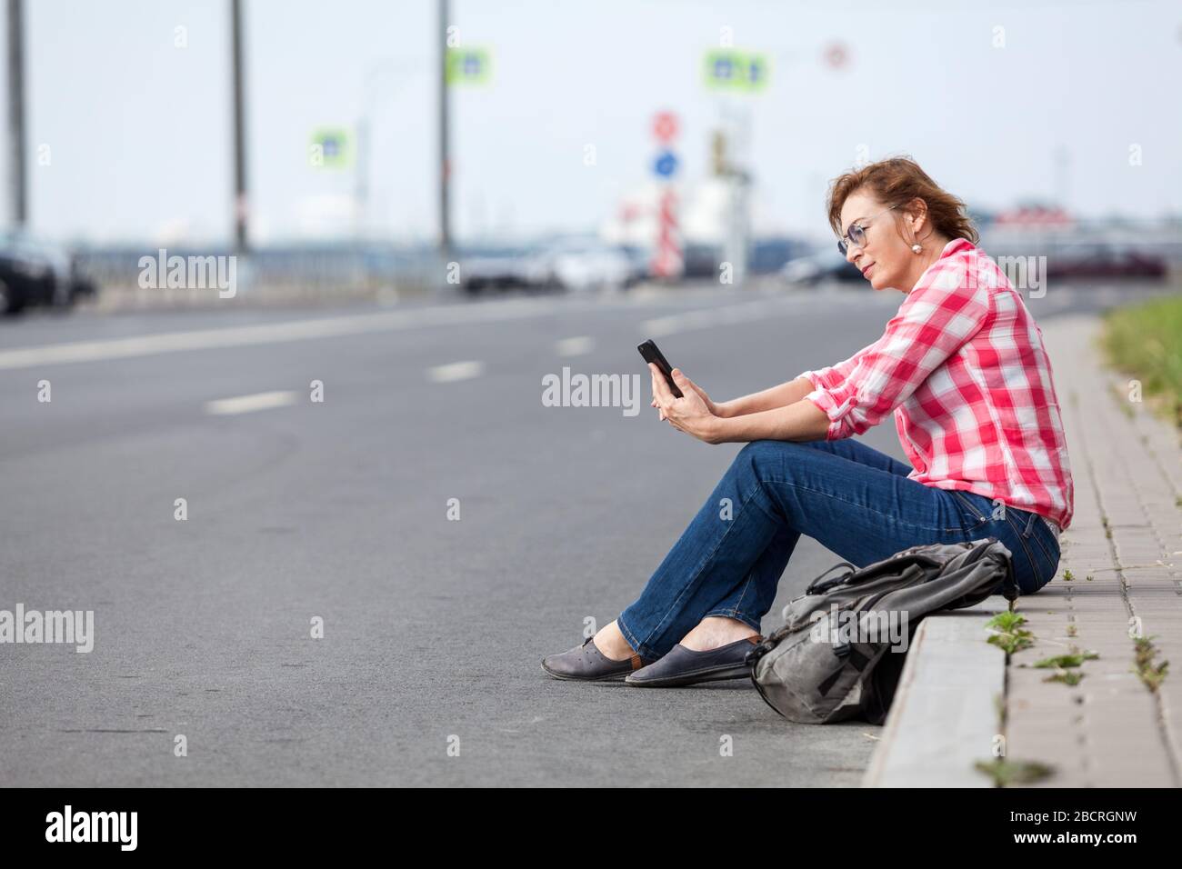 La donna di mezza età inizia a bloggarsi sulle strade della città, utilizzando smartphone, seduto sul lato della strada Foto Stock