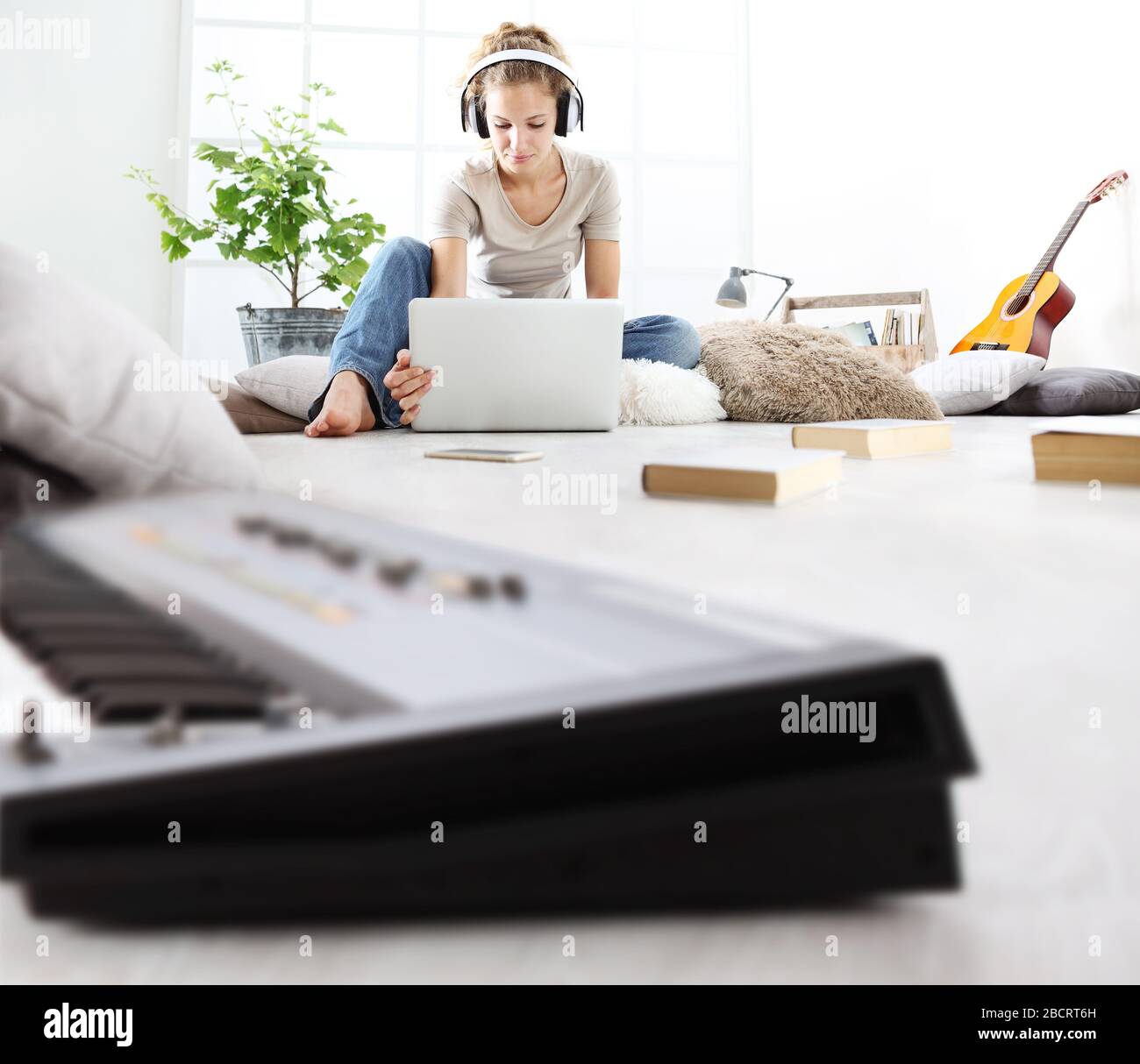 giovane donna seduta in soggiorno studiando musica con cuffie e computer, concetto di soggiorno a casa Foto Stock