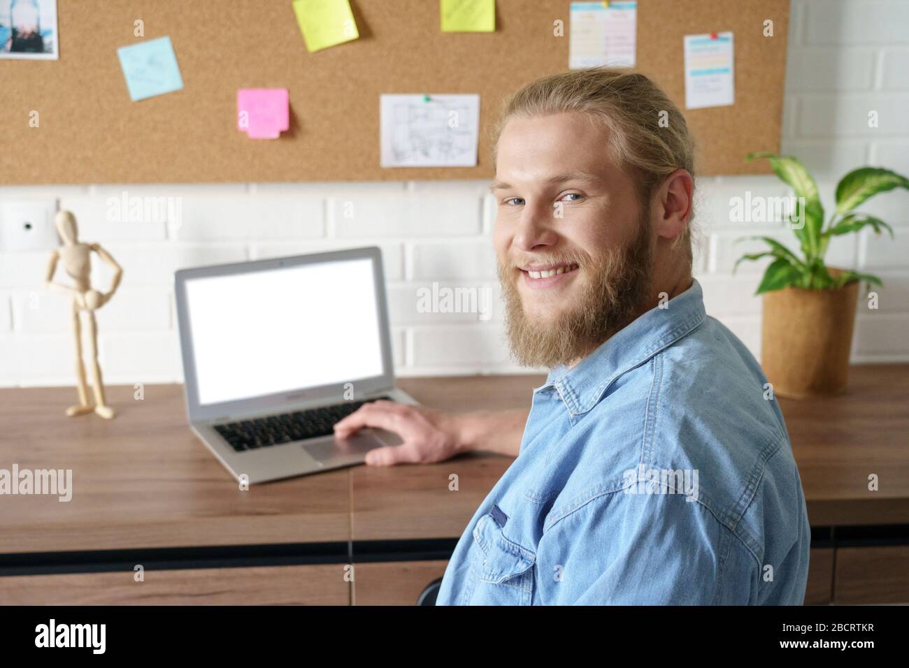 Uomo sorridente e millenario che guarda la macchina fotografica che lavora da casa su un notebook. Foto Stock