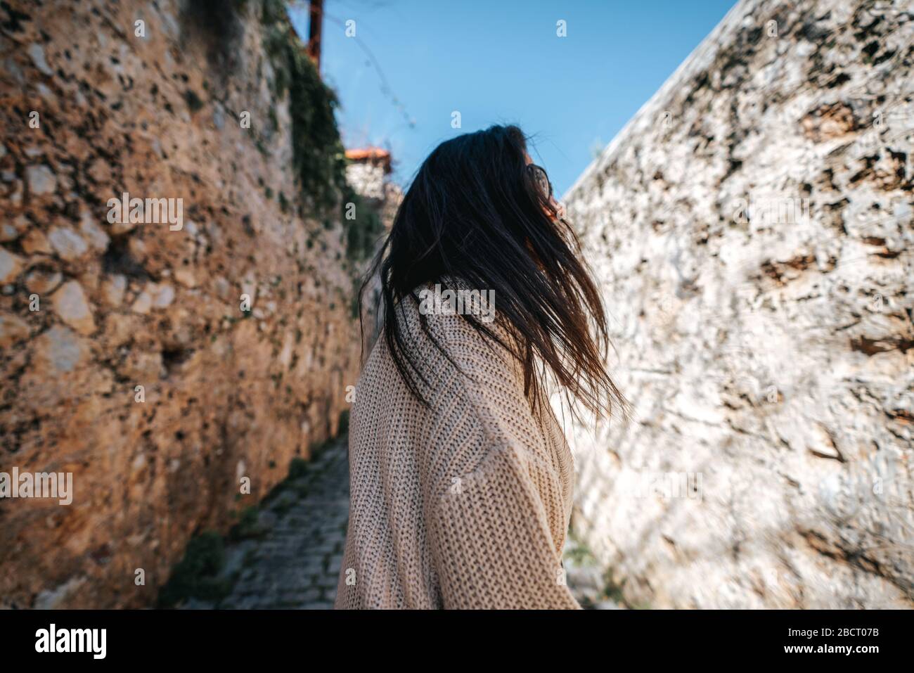 Giovane donna sta camminando con felicità tra mura storiche su uno stretto vicolo. Turismo e concetto di viaggio Foto Stock