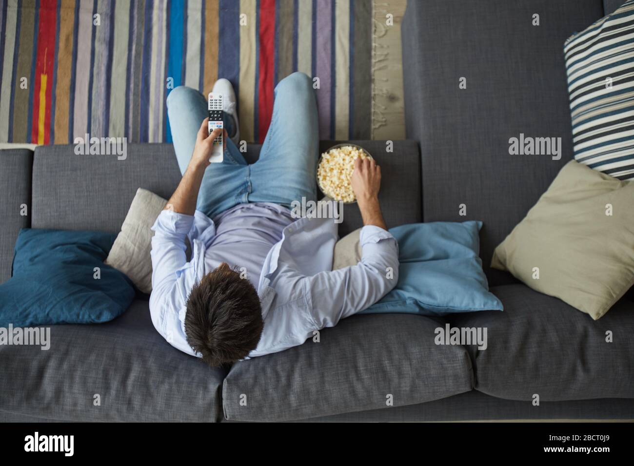 Direttamente sopra la vista a uomo maturo guardando la TV e tenendo ciotola di popcorn mentre si siede sul divano a casa, copia spazio Foto Stock