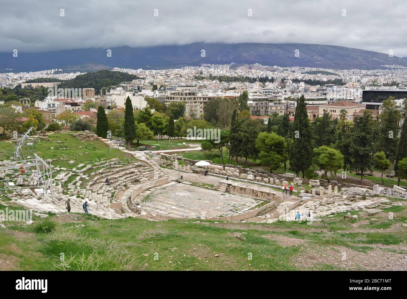 Atene, Grecia - 24 ottobre 2015: Antiche rovine greche del teatro di Dioniso, rovine in mezzo a verde lussureggiante erba. Vista dall'alto dell'Acropoli in una giornata nuvolosa. Foto Stock