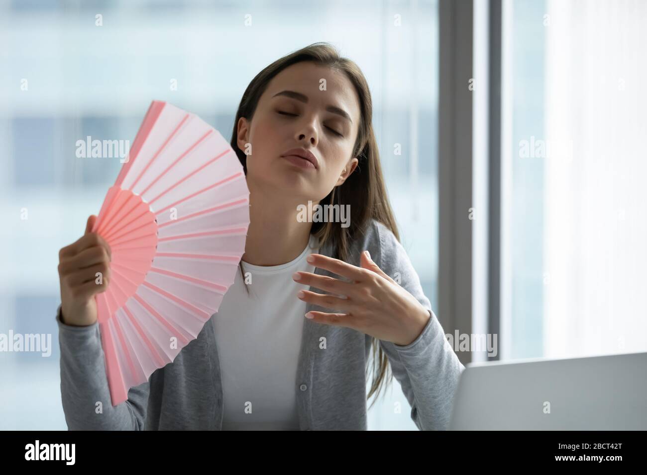 Un dipendente donna surriscaldato respira aria fresca dal ventilatore a mano Foto Stock
