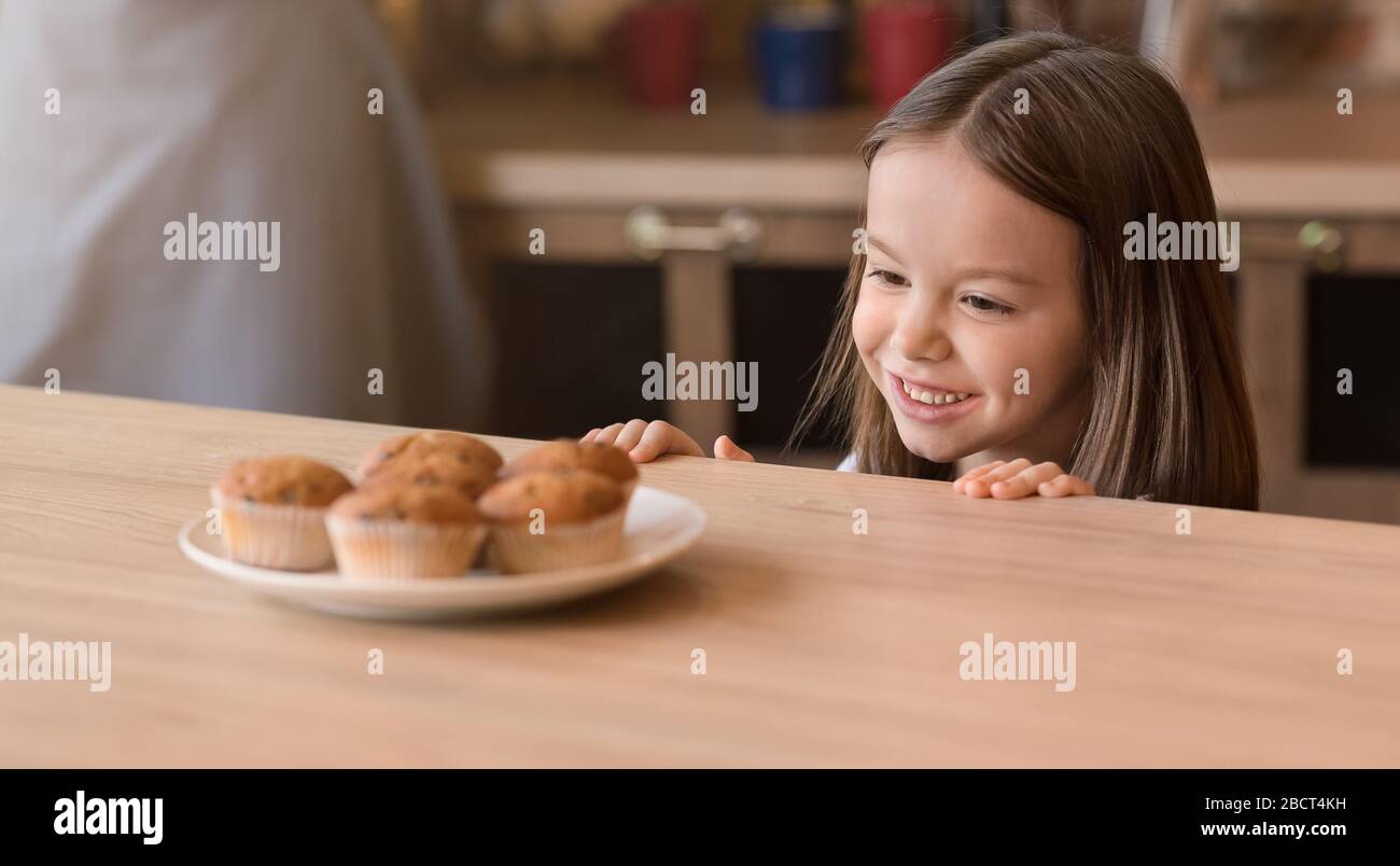 Concetto di bambini e dolci. Adorabile bambina che brama i biscotti, guardando i dolci in cucina, panorama con spazio per le copie Foto Stock