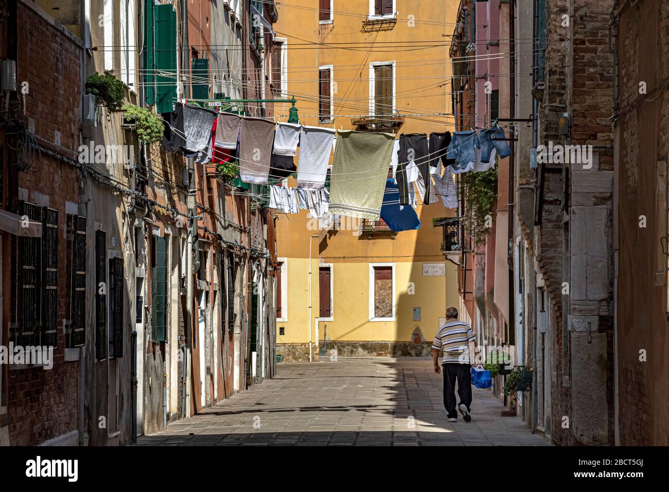 Un uomo cammina lungo Corte Calle colonne un piccolo cortile a Venezia, Italia con lavaggio appeso ad asciugare su una linea stretta tra case, Venezia Foto Stock