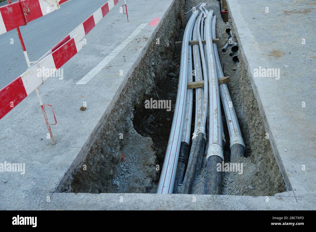 tubi in polipropilene spesso in una fossa di un edificio in una strada di cantiere di ingegneria civile con tavole di sbarramento rosse e bianche, Foto Stock