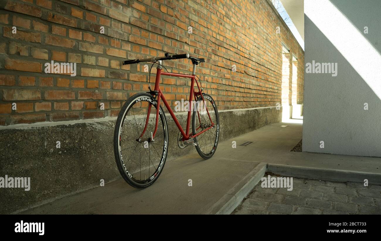 Bici a ingranaggi fissi in stile retrò rosso a singlespeed isolata su una parete in mattoni Foto Stock Bici a ingranaggi fissi in stile retrò rosso a singlespeed isolata su una parete in mattoni Foto Stock