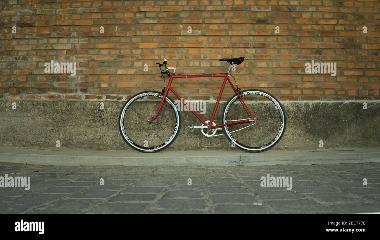 Bici a ingranaggi fissi in stile retrò rosso a singlespeed isolata su una parete in mattoni Foto Stock Bici a ingranaggi fissi in stile retrò rosso a singlespeed isolata su una parete in mattoni Foto Stock