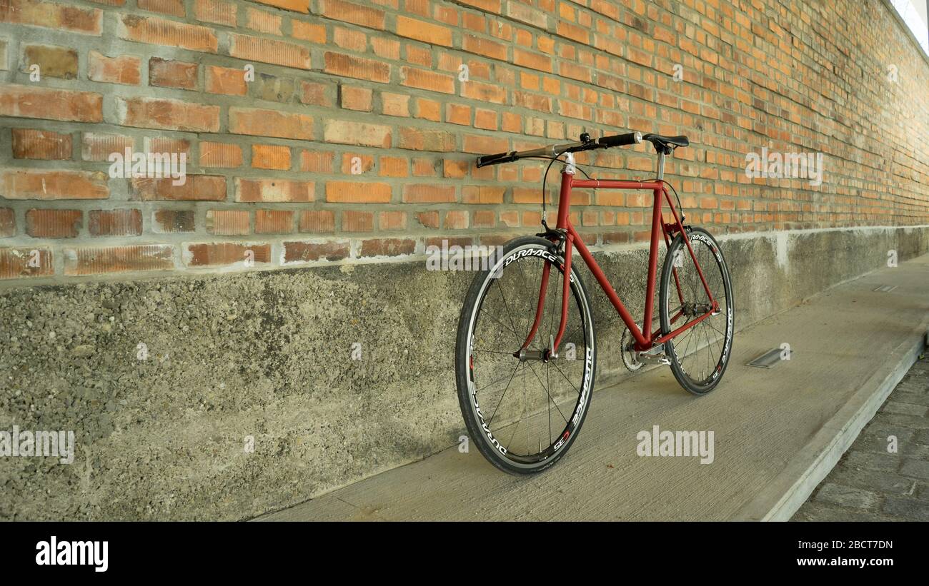 Bici a ingranaggi fissi in stile retrò rosso a singlespeed isolata su una parete in mattoni Foto Stock Bici a ingranaggi fissi in stile retrò rosso a singlespeed isolata su una parete in mattoni Foto Stock