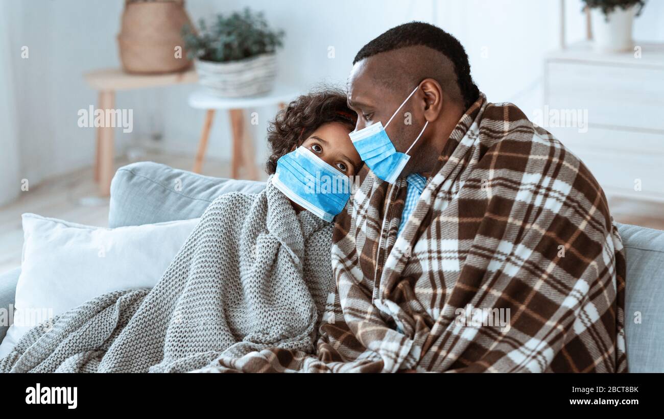 Pericolo di diffusione del virus. Famiglia Afro-americana che rimane a casa, indossando maschere protettive, spazio vuoto. Panorama Foto Stock