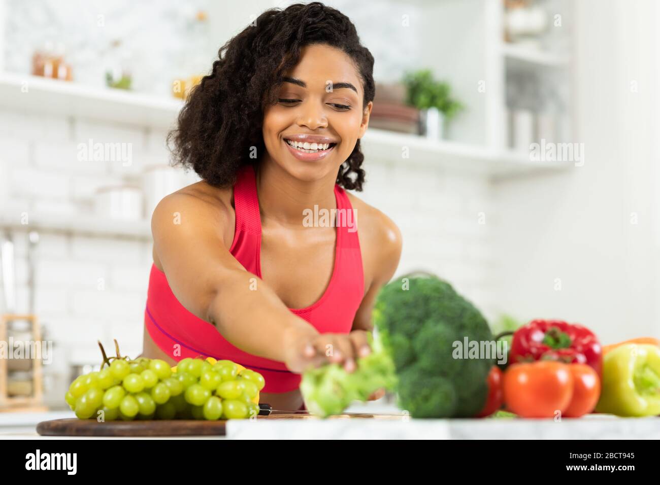 Felice giovane donna nera che prepara insalata di verdure Foto Stock