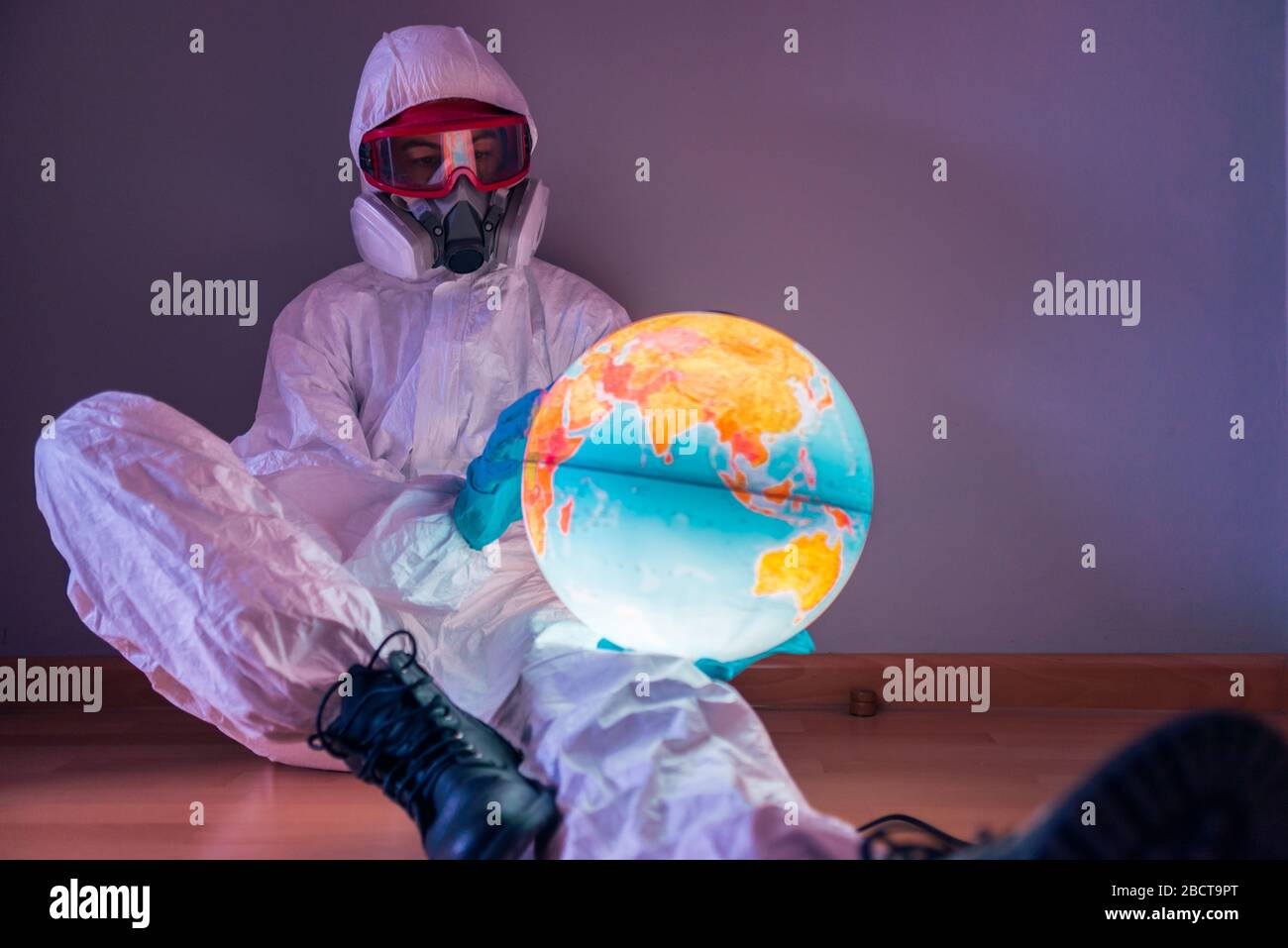 Concetto: Crisi virale mondiale. Donna in camice da laboratorio, guanti in nitrile, occhiali, maschera facciale e tuta NBC per coronavirus 19, seduta sul pavimento Foto Stock