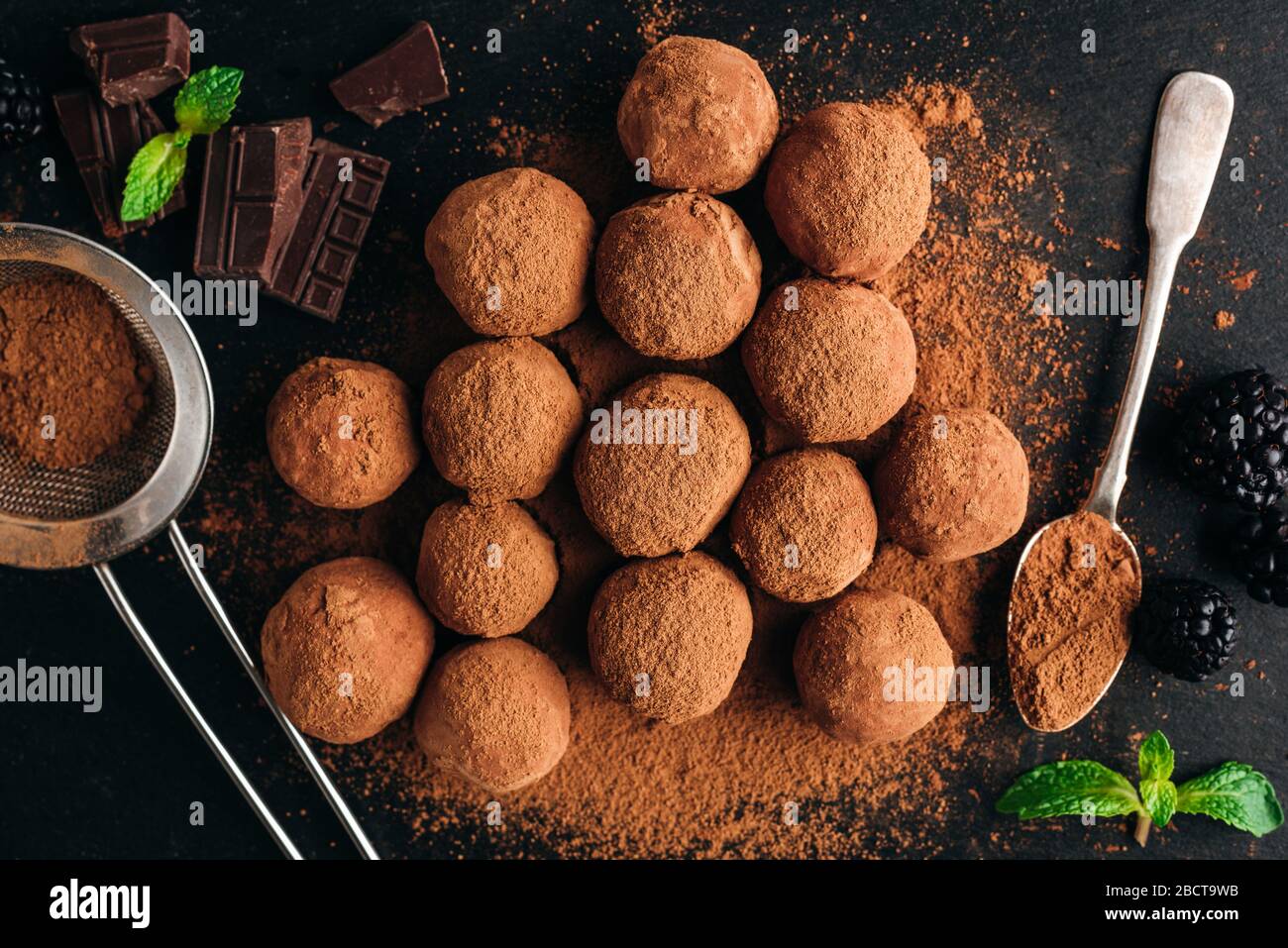Tartufi di cioccolato con polvere di cacao su fondo di ardesia nera. Vista dall'alto del tavolo. Caramelle al cioccolato fatte in casa Foto Stock