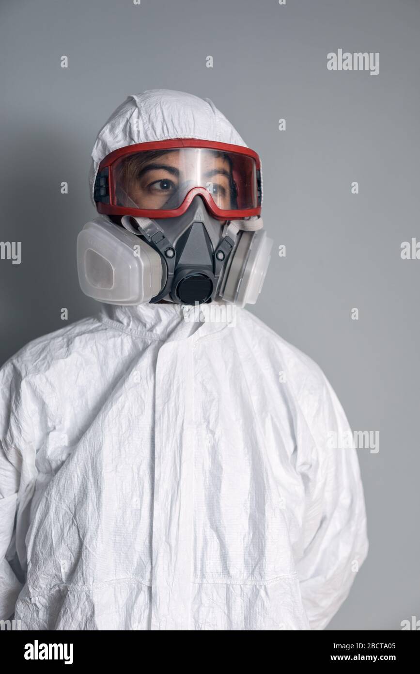 Ritratto di donna in camice da laboratorio, guanti in nitrile, occhiali, maschera facciale e tuta protettiva NBC con sfondo grigio. Foto Stock
